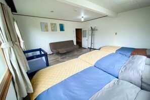 A room with a sofa, two beds with patterned bedding, a coat rack, and a door leading to another room. - Sola st. Inn Noboribetsu (Noboribetsu)