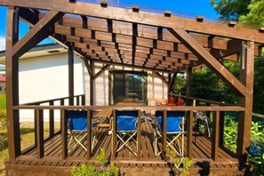 A wooden deck with a pergola, blue outdoor seating, and a view of a building in the background. - Sola st. Inn Noboribetsu (Noboribetsu)