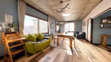 Una habitación con piso de madera, un sofá verde, una mesa de comedor y un ventanal grande.