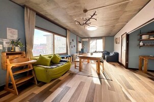 Una habitación con piso de madera, un sofá verde, una mesa de comedor y un ventanal grande.