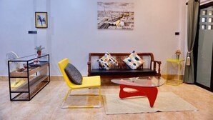 A modern living room with a sofa, a yellow chair, a glass coffee table, and a black metal shelf unit. - P'Ja House by Lorenzo Property (Hat Yai)