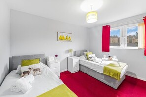 Une chambre d’hôtel avec deux lits, une fenêtre avec des rideaux rouges, un tableau au mur et une moquette rouge.