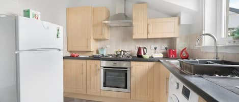 Une cuisine moderne avec des meubles en bois, un four encastré, un lave-linge et une fenêtre qui laisse entrer la lumière naturelle.