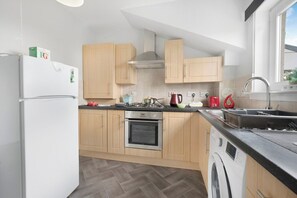 A modern kitchen with wooden cabinets, a built-in oven, a washing machine, and a window providing natural light.