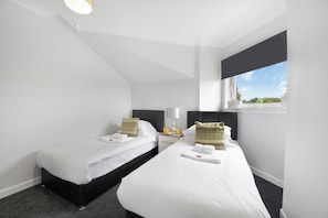 Een hotelkamer met twee enkele bedden, een klein nachtkastje met een lamp en een raam met uitzicht.
