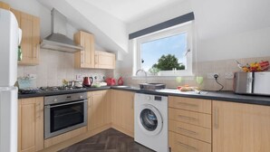 A compact kitchen with a built-in oven, a washing machine, and a window providing natural light.