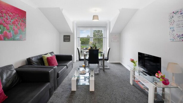 A modern living room with a black leather sofa, a glass coffee table, and a dining area with a white table and chairs.
