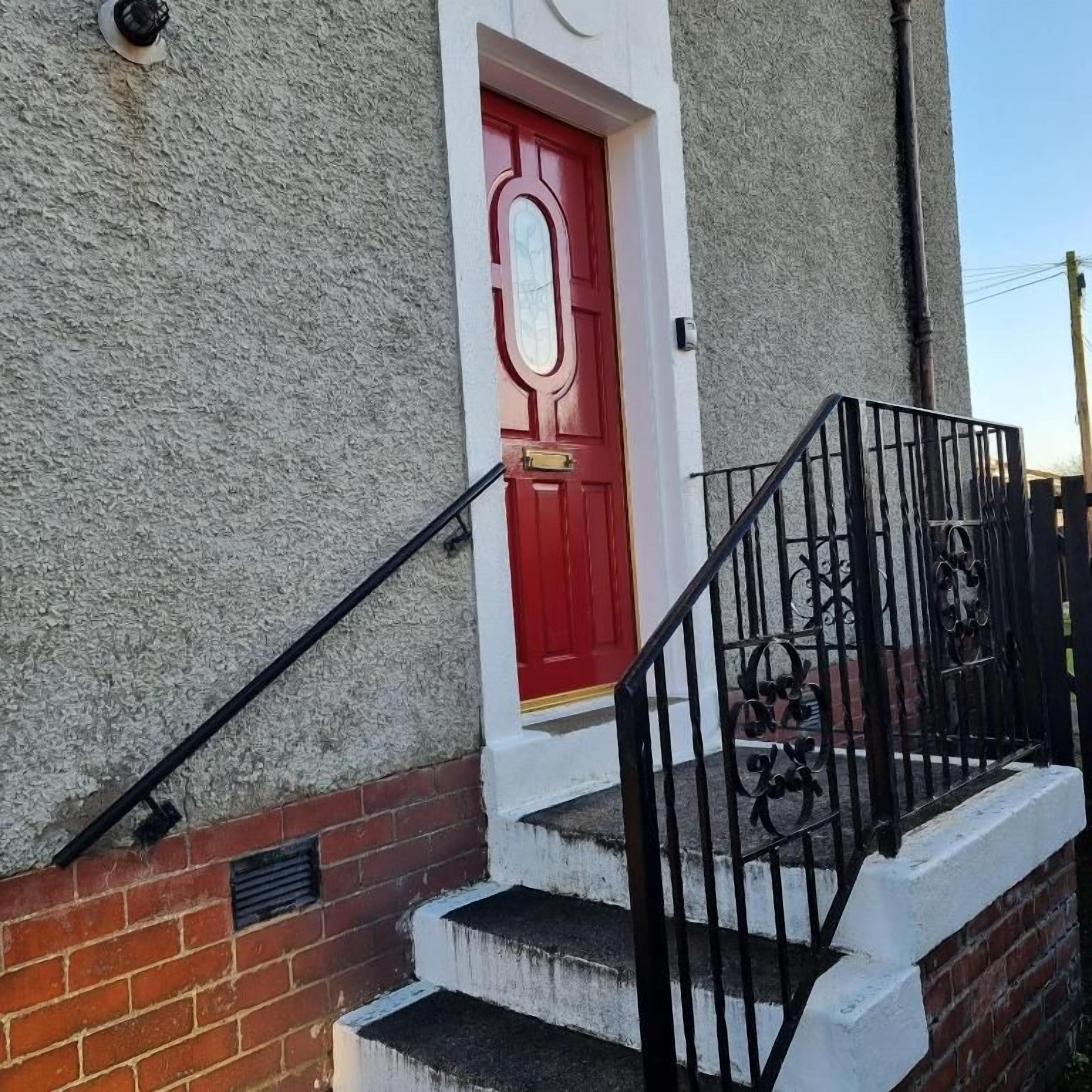 A red door with a white frame, a brick wall, and a black metal staircase with a handrail.