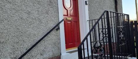 A red door with a white frame, a brick wall, and a black metal staircase with a handrail.