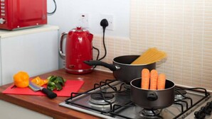 Une cuisine équipée d’une cuisinière, de casseroles, d’une bouilloire rouge et de légumes disposés sur le plan de travail.