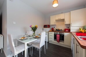 Une cuisine moderne avec des meubles blancs, une table à manger avec des chaises, un micro-ondes rouge et un évier.