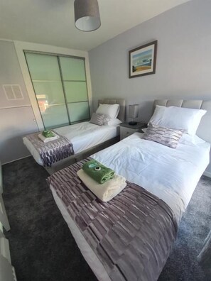 A hotel room with two beds, a sliding door, a bedside table with a lamp, and a painting on the wall.