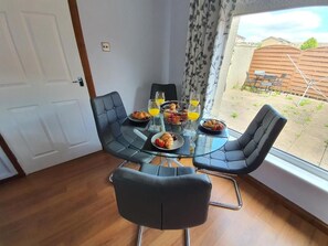A dining table with chairs, a glass top, and food and drinks.