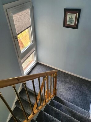 A carpeted staircase with a wooden handrail, a door with a window, and a framed picture on the wall.