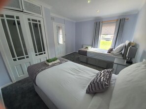 Une chambre avec deux lits, une armoire, une fenêtre avec des rideaux et une table de chevet avec une lampe.