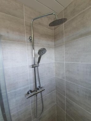 Une douche équipée d’un pommeau de douche à main et d’une douchette à pluie fixée au plafond, le tout installé dans une salle de bain carrelée.