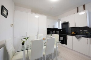 Una cocina moderna con armarios blancos, una mesa de comedor de vidrio y una encimera negra.