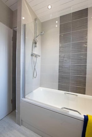 A modern bathroom with a glass-enclosed shower, a white bathtub, and a tiled wall.