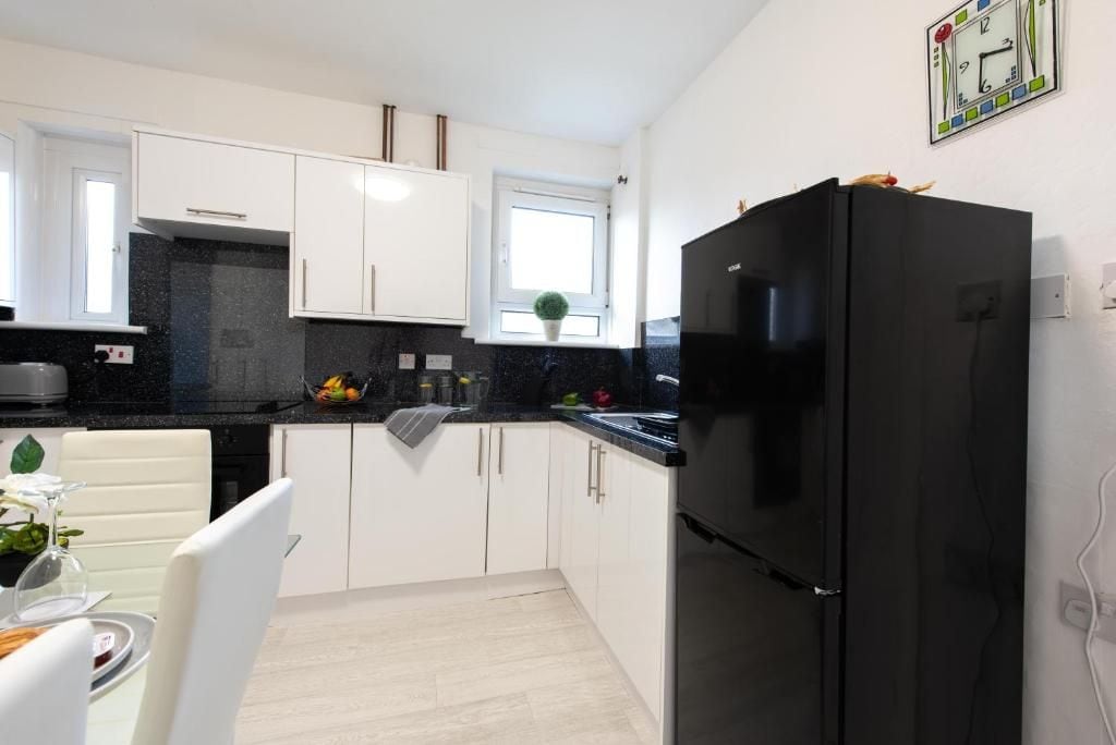 Une cuisine de taille réduite avec des meubles blancs, un réfrigérateur noir et une fenêtre.