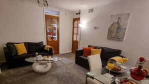 A living room with a black sofa, a glass coffee table, and a dining table set with breakfast items. - Premier - Whifflet Apartment (North Lanarkshire)