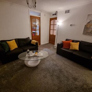 A living room with two black sofas, a glass coffee table, and a lamp.