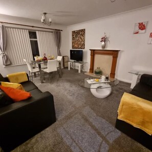 A living room with a sofa, a coffee table, a TV, and a fireplace.