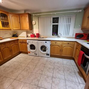 A kitchen with wooden cabinets, a washing machine, a microwave, and a sink.