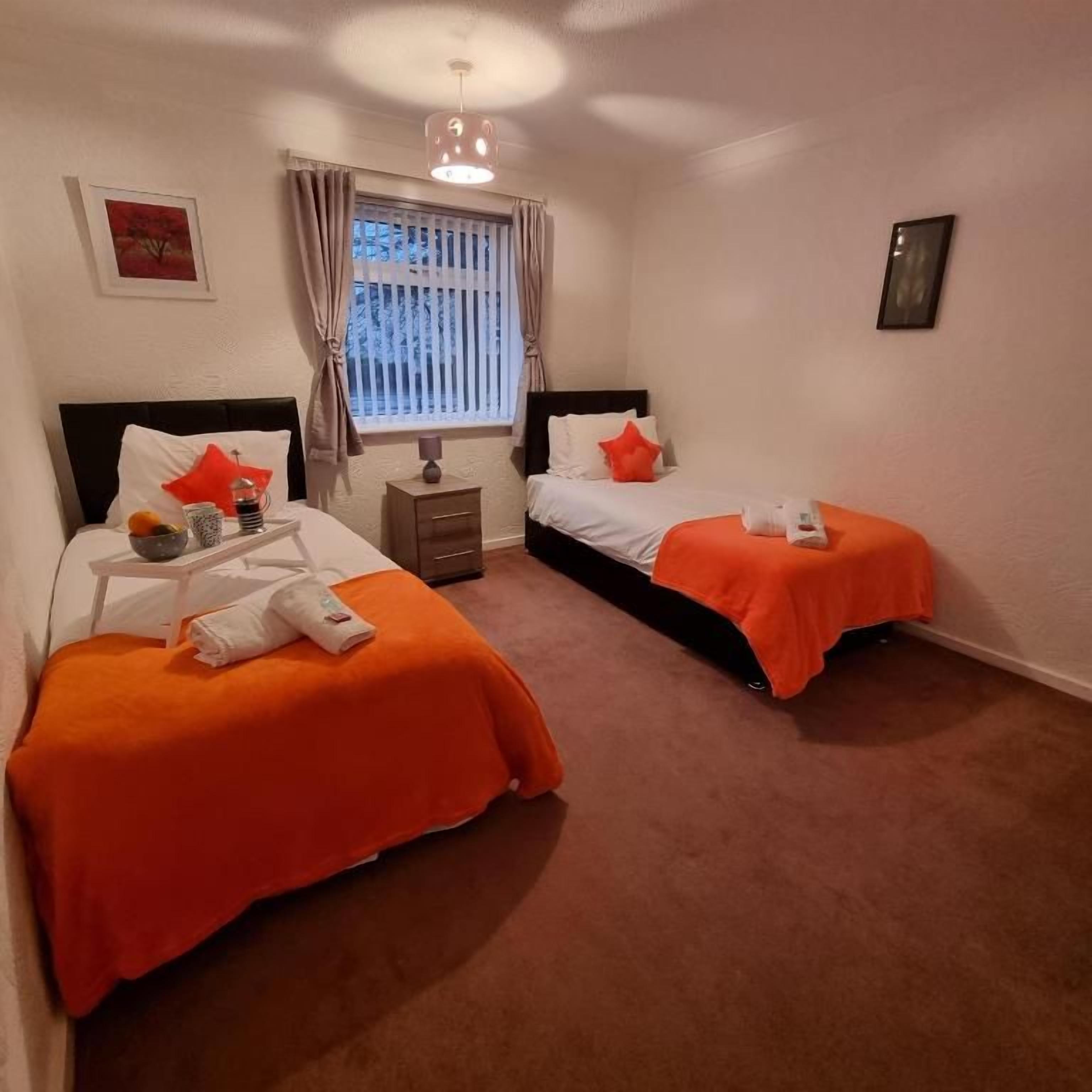 A hotel room with two beds, a nightstand, a window with curtains, and a wall-mounted picture.