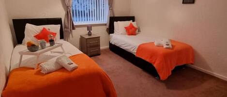 A hotel room with two beds, a nightstand, a window with curtains, and a wall-mounted picture.