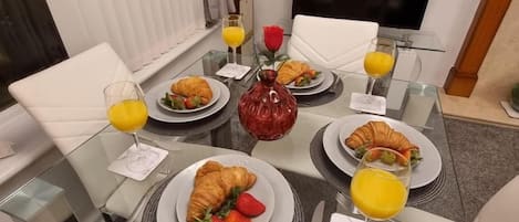 A breakfast setting with a glass table, plates of croissants and fruit, and glasses of orange juice.