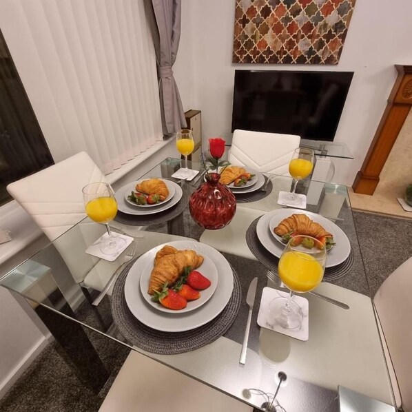 A breakfast setting with a glass table, plates of croissants and fruit, and glasses of orange juice.