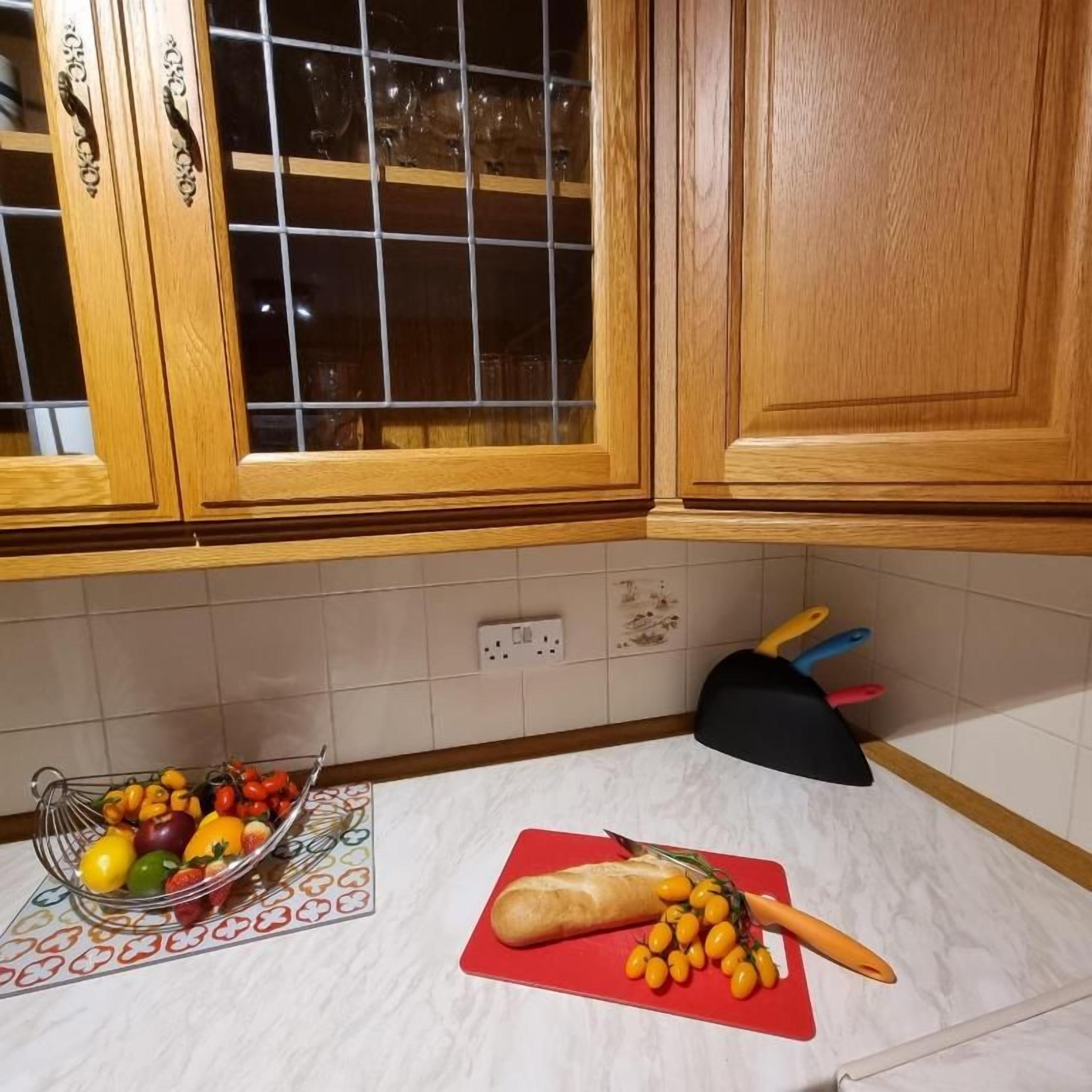 A kitchen with wooden cabinets, a fruit bowl, a cutting board with vegetables, and a knife block.