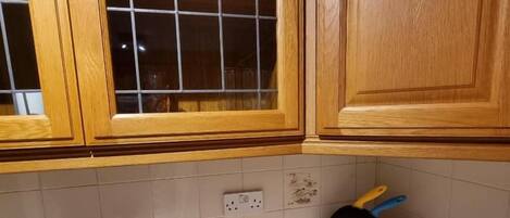 A kitchen with wooden cabinets, a fruit bowl, a cutting board with vegetables, and a knife block.
