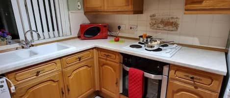 A compact kitchen with wooden cabinets, a microwave, a stove, and a washing machine.