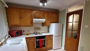 A compact kitchen with wooden cabinets, a white sink, a red microwave, a white refrigerator, and a tiled floor. - Premier - Whifflet Apartment (North Lanarkshire)