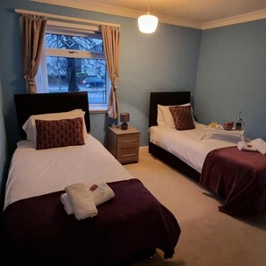 A hotel room with two beds, a nightstand, a window with curtains, and a hanging light fixture.