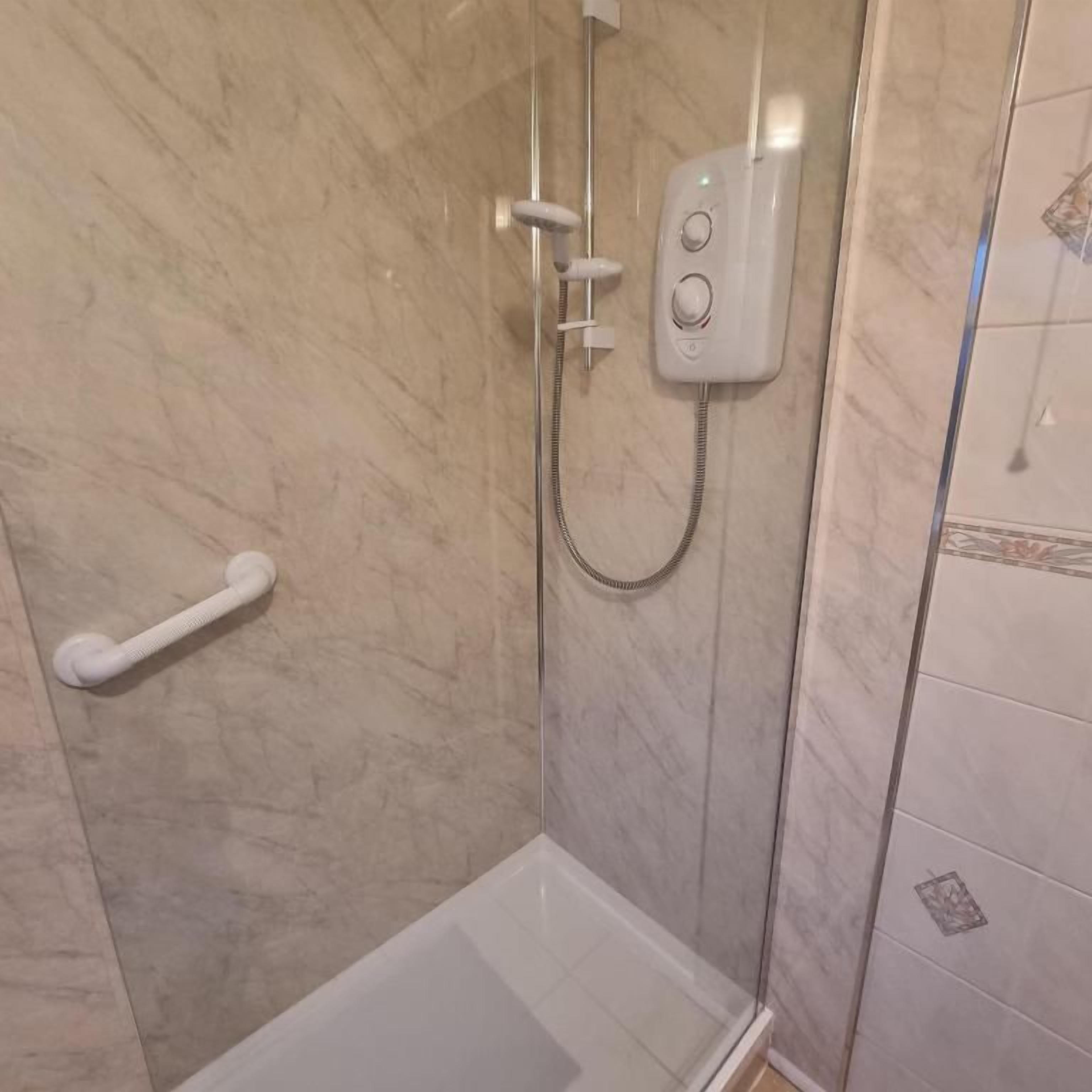A shower area with a glass enclosure, a handheld showerhead, and a wall-mounted control panel.