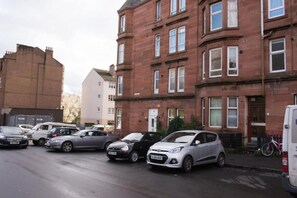 Une rangée de voitures garées le long d’une rue, avec un immeuble en briques rouges et un immeuble blanc en arrière-plan.