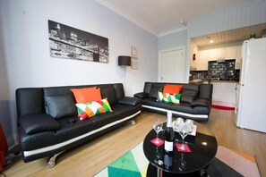 Un salon moderne avec deux canapés noirs, une table basse sur laquelle sont posés des verres à vin, et un tableau représentant un paysage urbain accroché au mur.