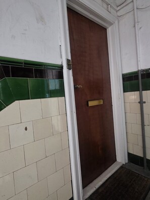 Une porte dotée d’une poignée en laiton, des murs recouverts de carreaux blancs rehaussés de touches de vert et un cadre de porte en métal.