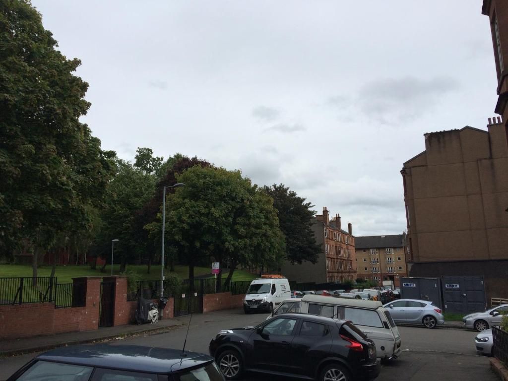 A parking area with multiple cars, a building with a flat roof, and a tree-lined street.