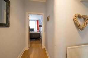A hallway with a wooden floor, a white radiator, and a heart-shaped decoration on the wall.