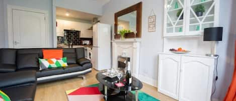 A living room with a black sofa, a colorful rug, a fireplace, and a kitchen in the background.