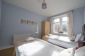 A bedroom with two beds, a radiator, a window with curtains, and wall decorations.