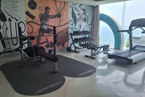 A gym with exercise equipment, a treadmill, and a wall with fitness-themed artwork. - Aparthotel in A La Carte - 2 bedrooms, balcony, beachfront, rooftop pool, central (Da Nang)