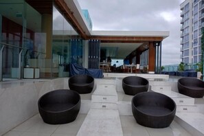 Outdoor seating with wicker chairs, a covered area, and a modern building with glass and wood elements. - Aparthotel in A La Carte - 2 bedrooms, balcony, beachfront, rooftop pool, central (Da Nang)