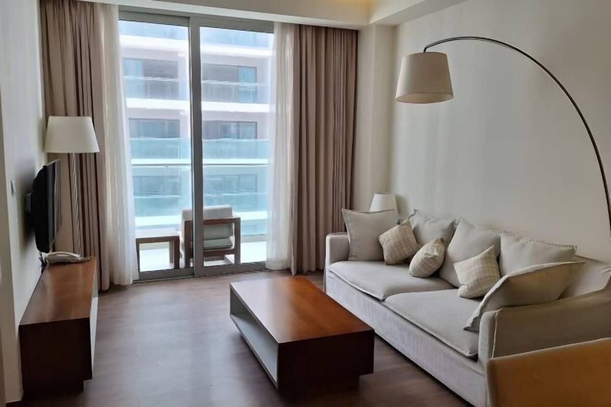 A modern hotel room with a sofa, a coffee table, a TV, and a lamp.