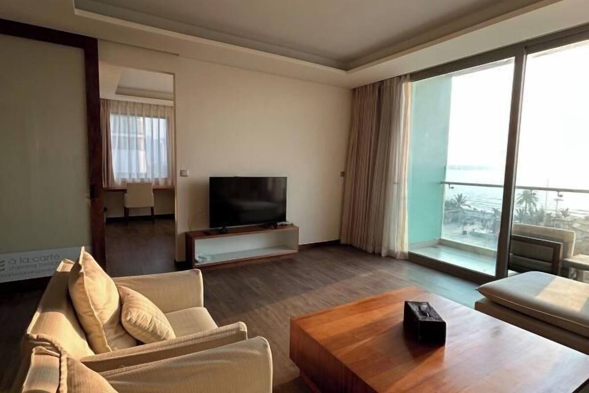 A hotel room with a TV, a sofa, a wooden coffee table, and a balcony with a view.