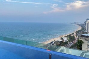 Une vue sur la côte depuis un balcon, avec un ciel dégagé, une plage et un pont situé au loin.