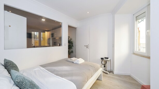 A bedroom with a bed, a large mirror, a door leading to a bathroom, and a window. - Suprema loft l (Lisboa)